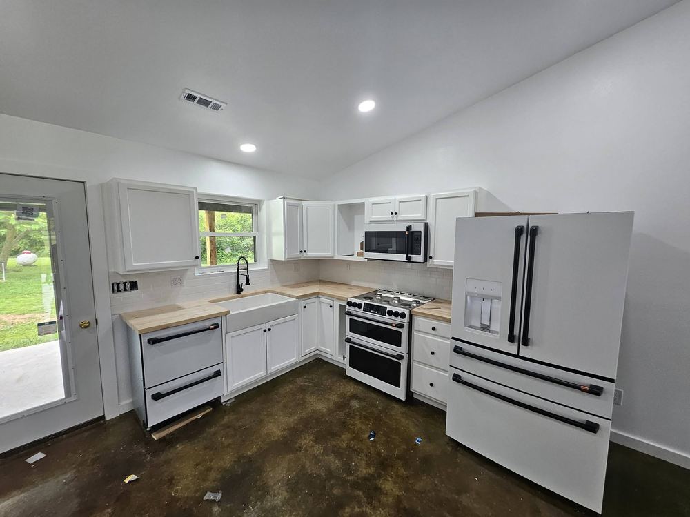 Finished kitchen with white cabinets, butcher block counters and a farmhouse sink