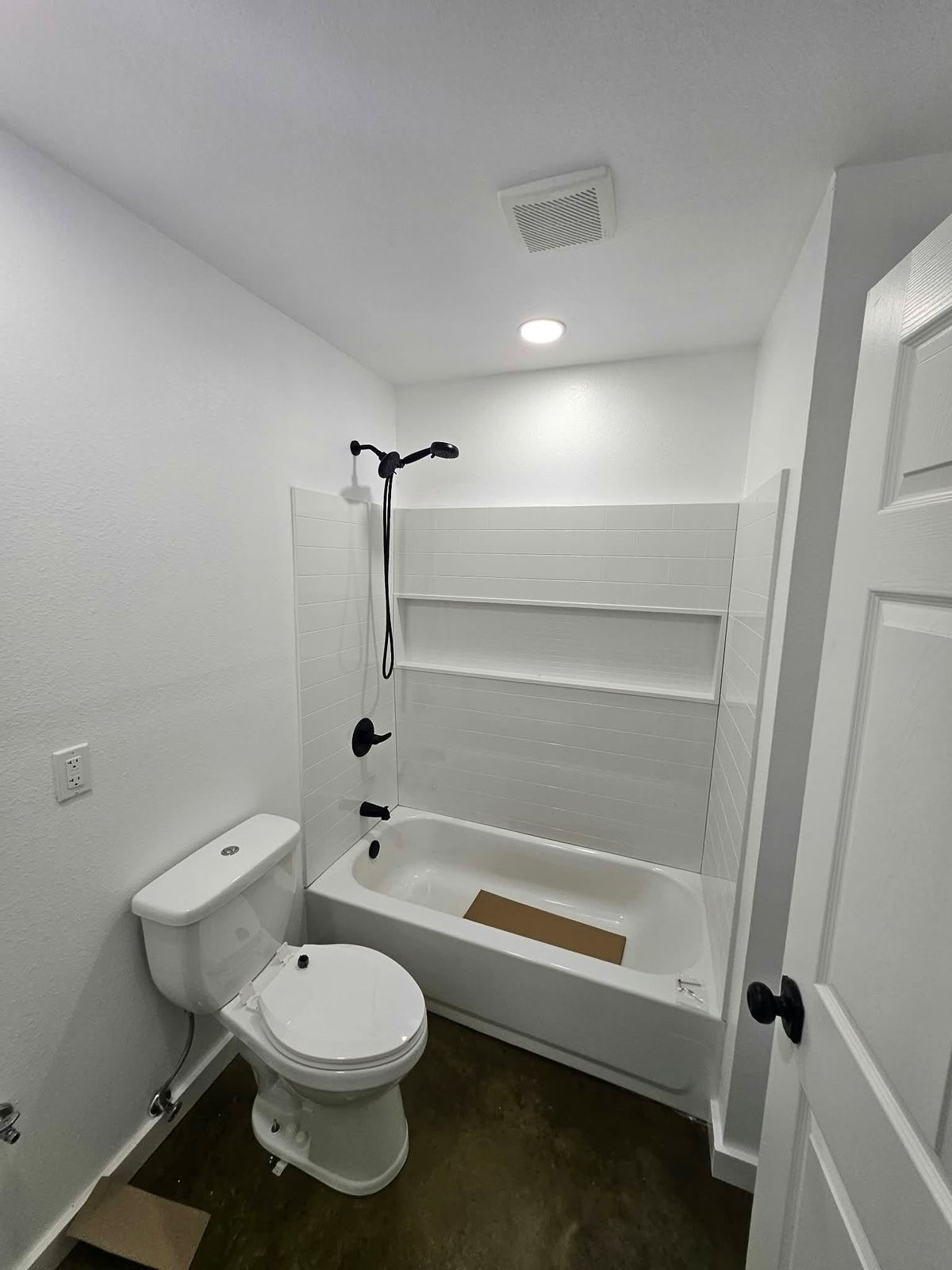 Remodeled bathroom with a white tiled tub surround, recessed shelf and black fixtures