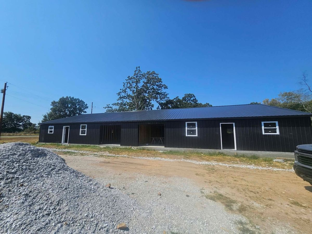 Long black metal warehouse with a standing seam roof and white-trimmed doors and windows