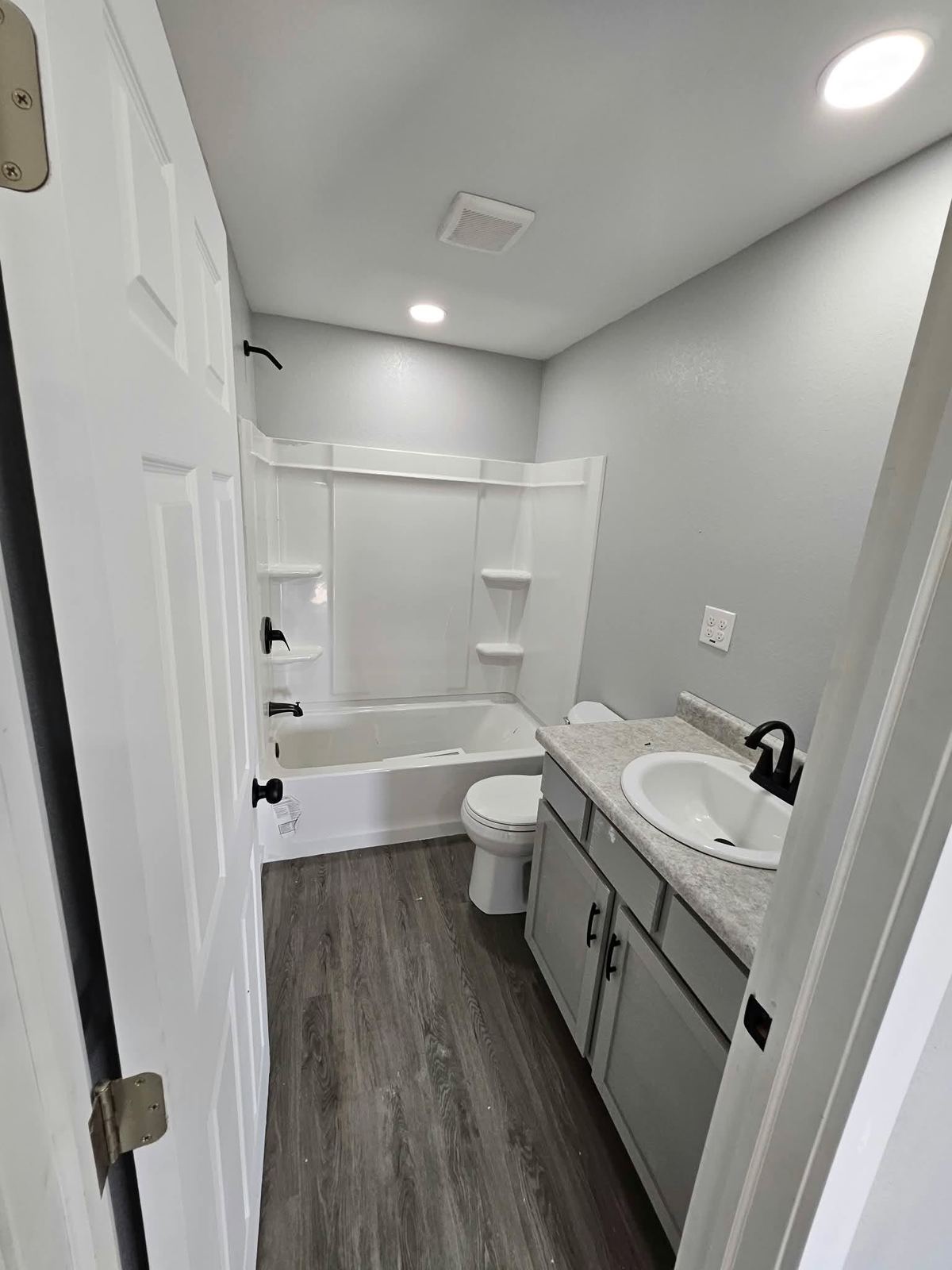 Finished bathroom with a gray vanity, tub surround and wood-look vinyl flooring