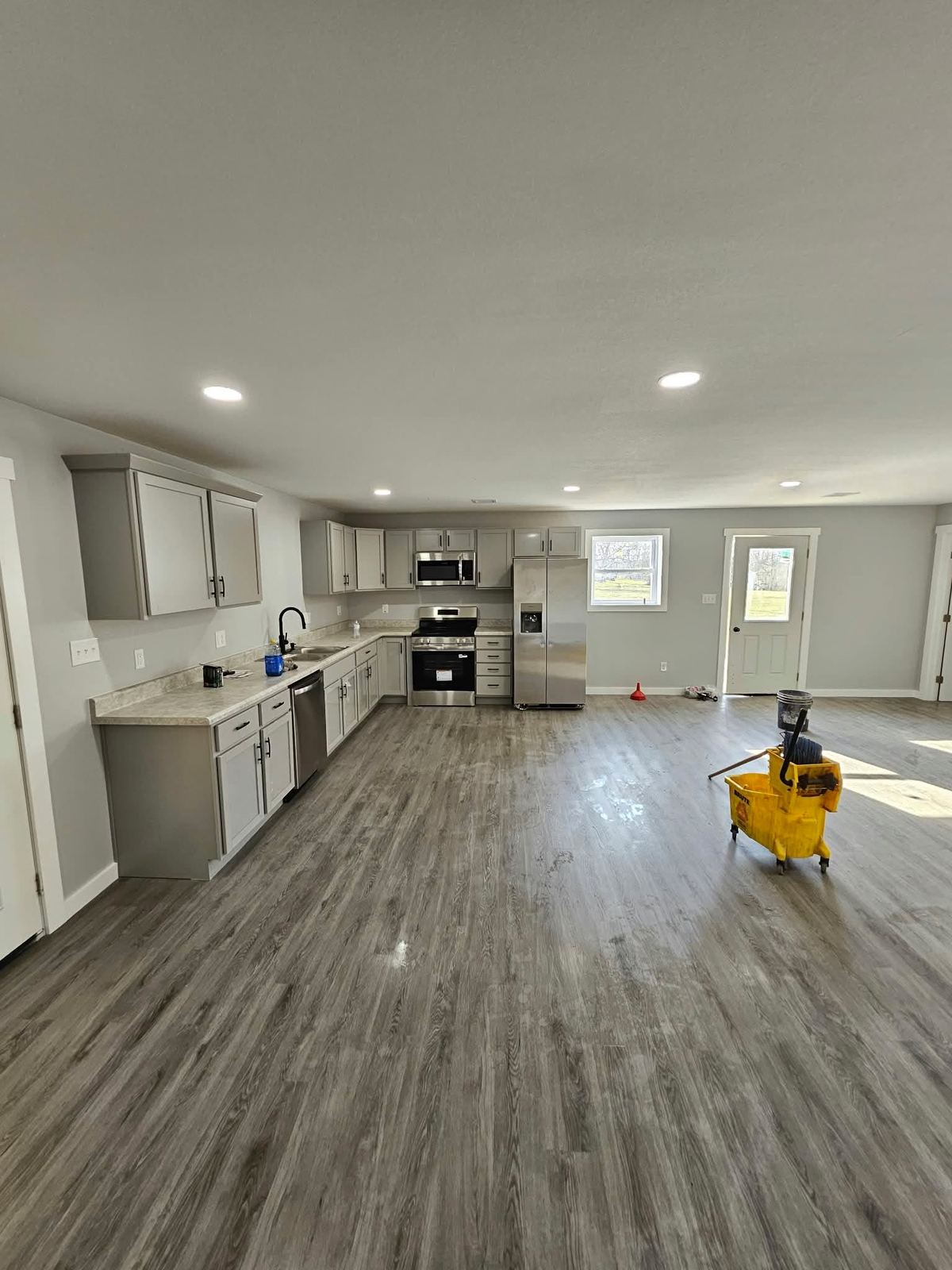 Open-plan kitchen with gray cabinets, stainless appliances and new vinyl plank flooring