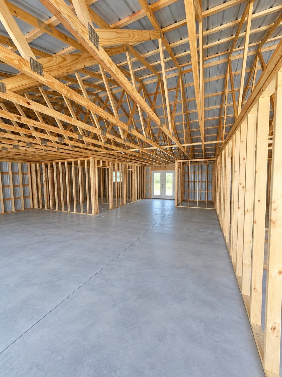 Interior of a post-frame building framed out with wood studs and roof trusses over a poured slab