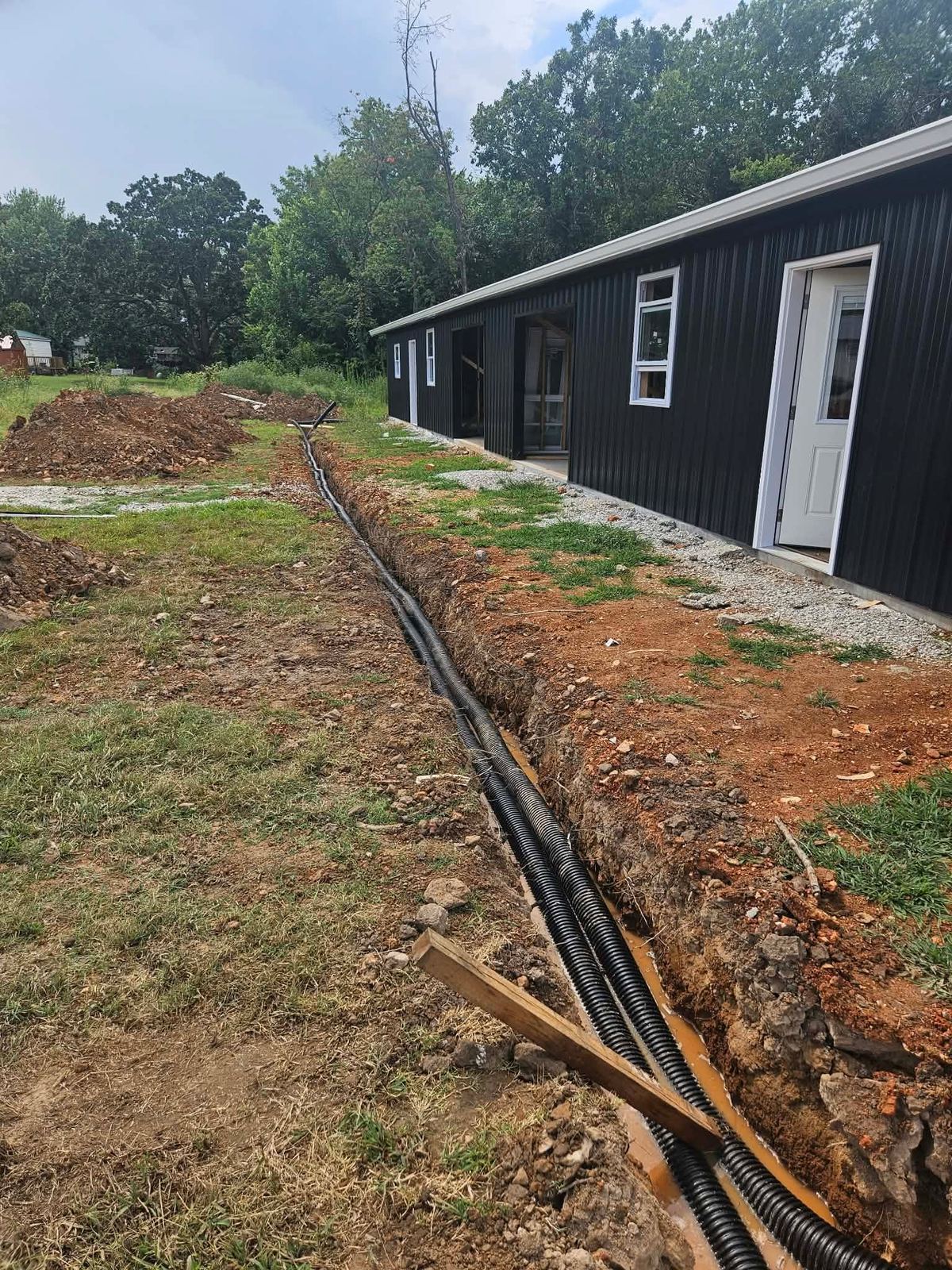 Open trench with conduit runs alongside a new black metal building